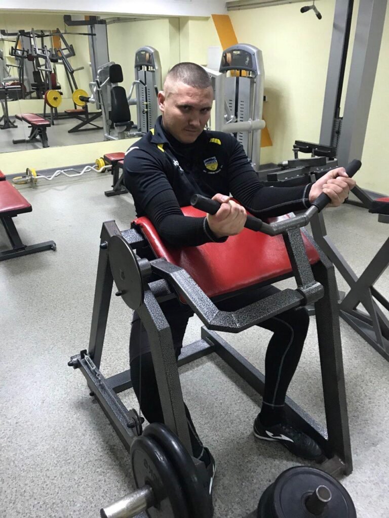 Юрій Гур виконує вправу на біцепс на тренажері у спортивній залі